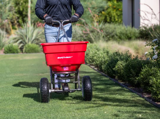 Man pushing an Earthway Spreader on lush green grass
