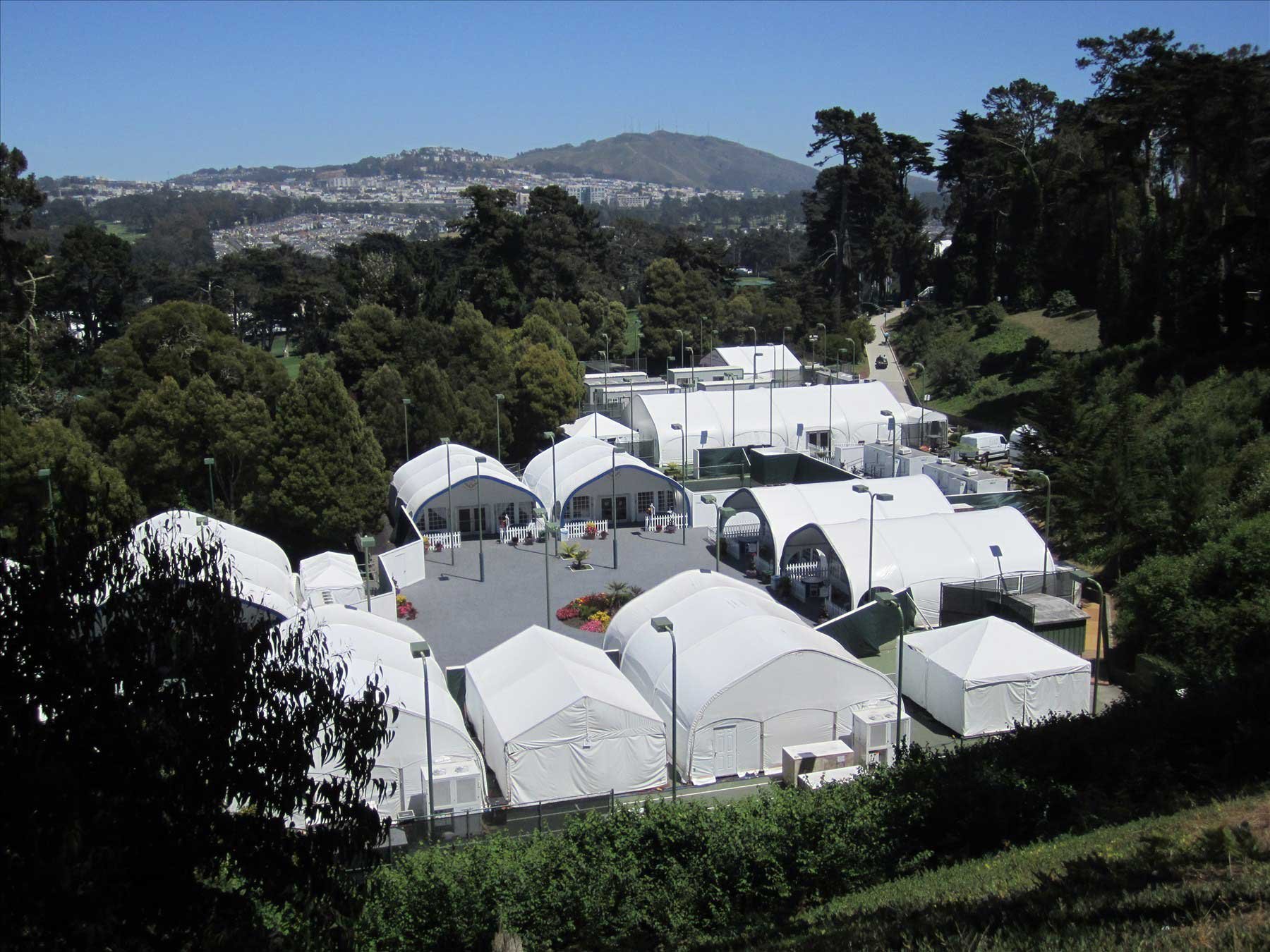 A group of white tents for people to assemble surrounded by green trees. 