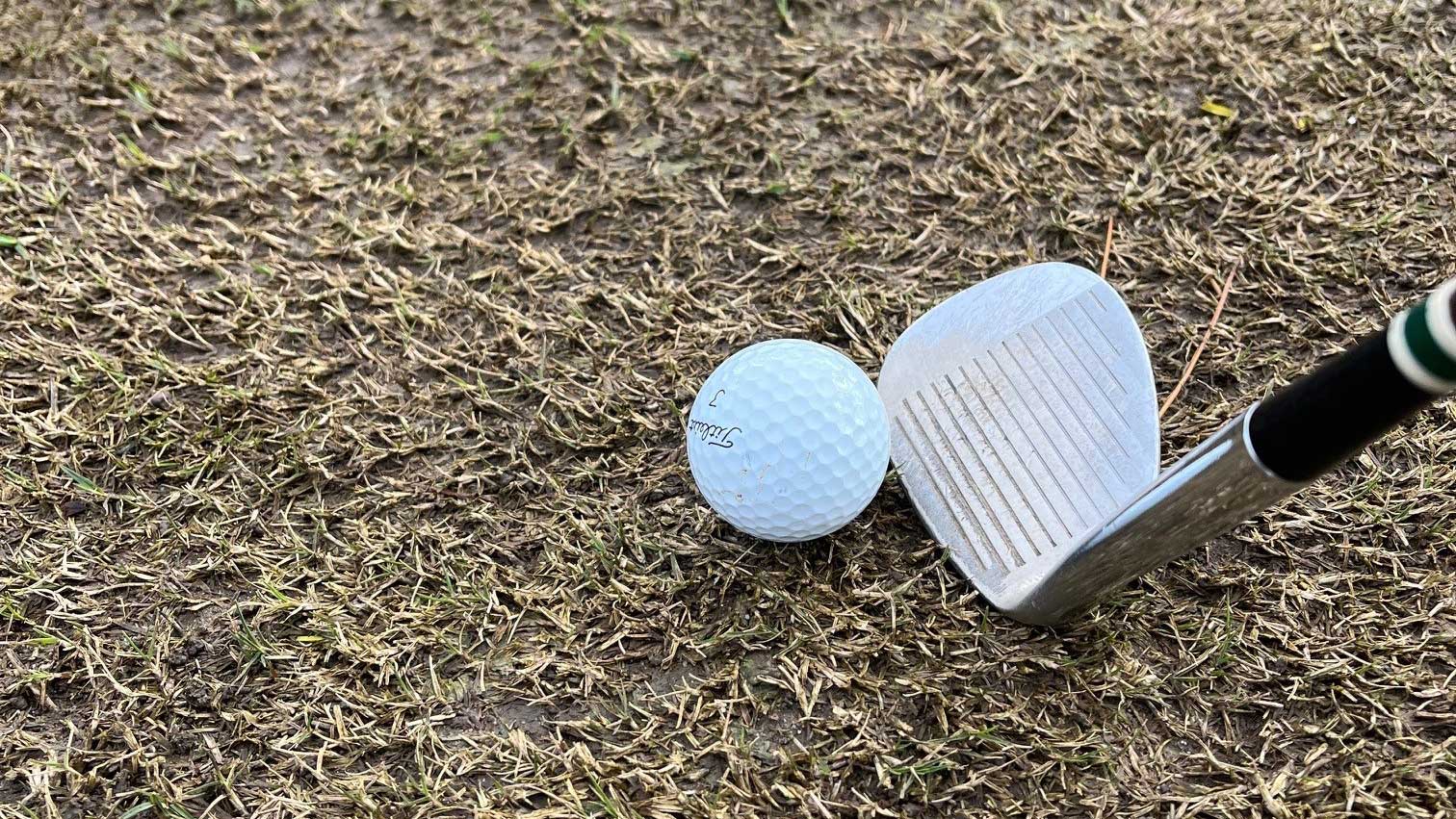 White golf ball and silver and black golf club on winter turf.
